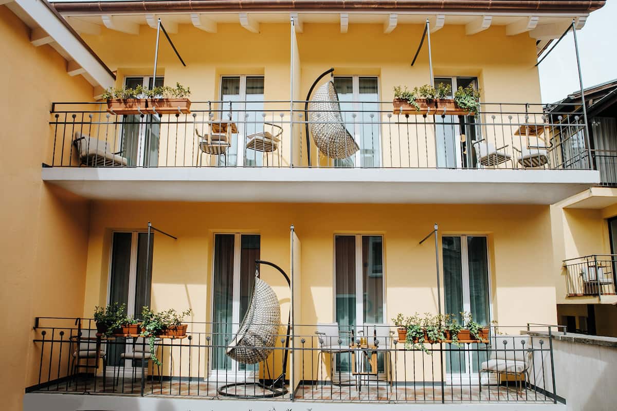 Un edificio de dos pisos con balcones, plantas en macetas y mobiliario exterior.
