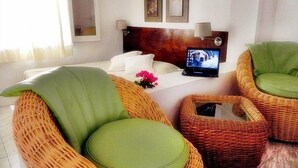 Um quarto com móveis de vime, um laptop sobre a mesa e uma cama com roupa de cama branca.
