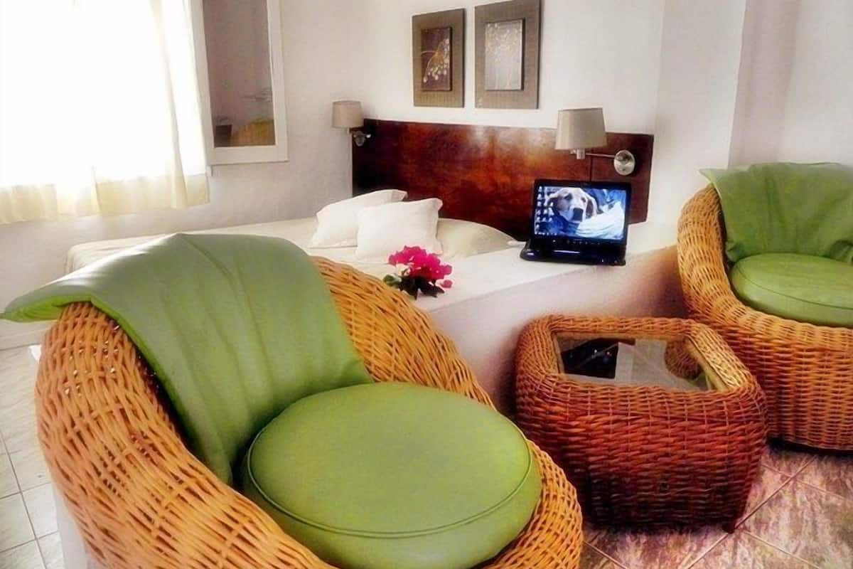 Una habitación con muebles de mimbre, una laptop sobre una mesa y una cama con ropa blanca.
