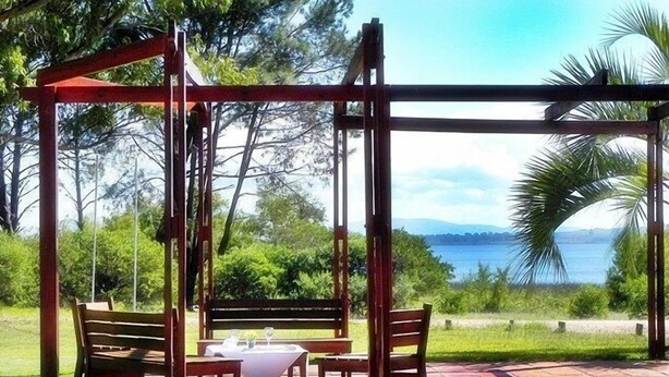 Um conjunto de baloiço de madeira com uma mesa e cadeiras numa área de jardim com vista para o mar.