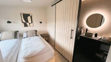A modern bedroom with a bed, bedside tables, a wardrobe, a bathroom with a sink and mirror.