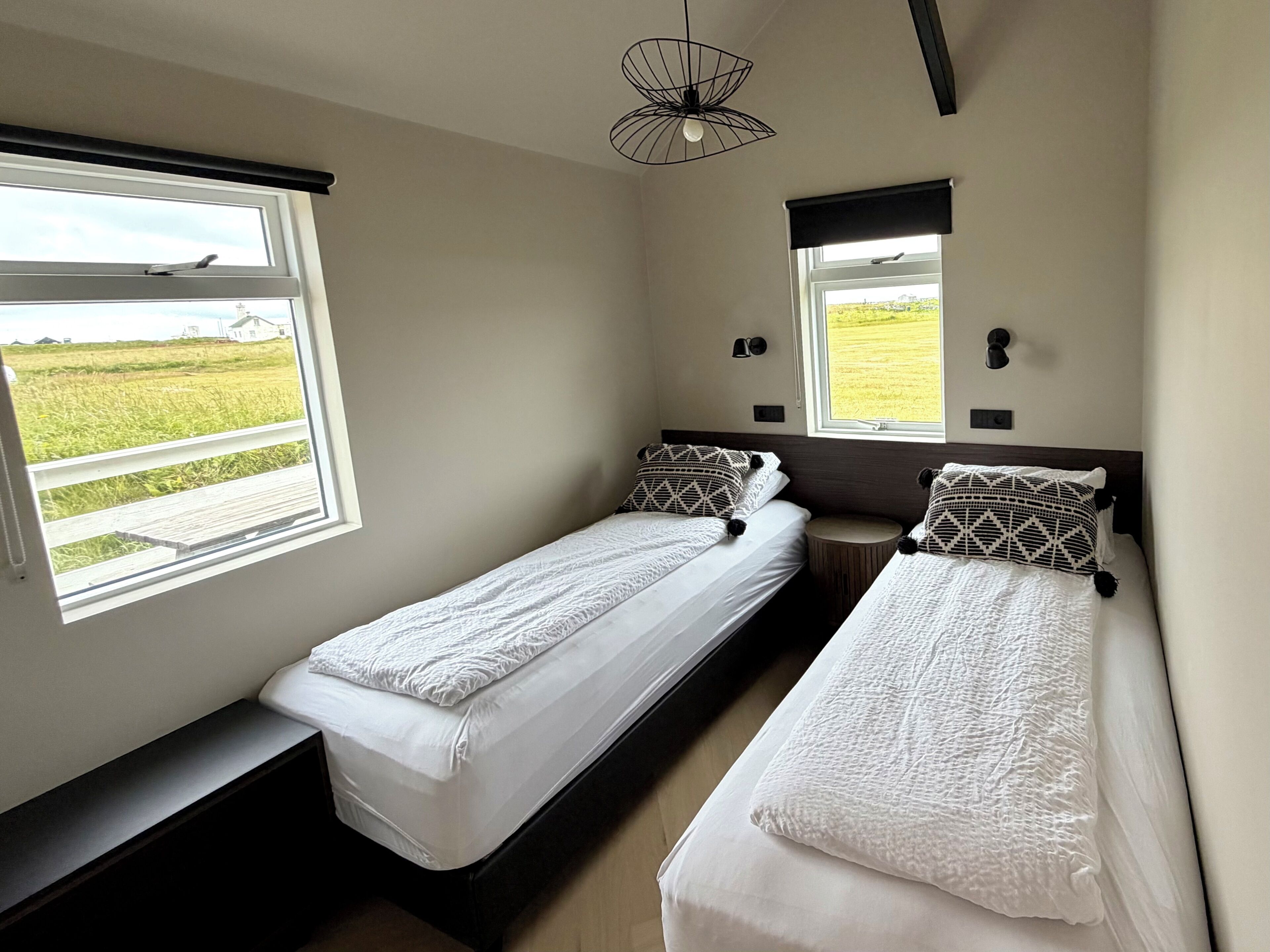 A room with two single beds, a bench, and a window with a view of a field.