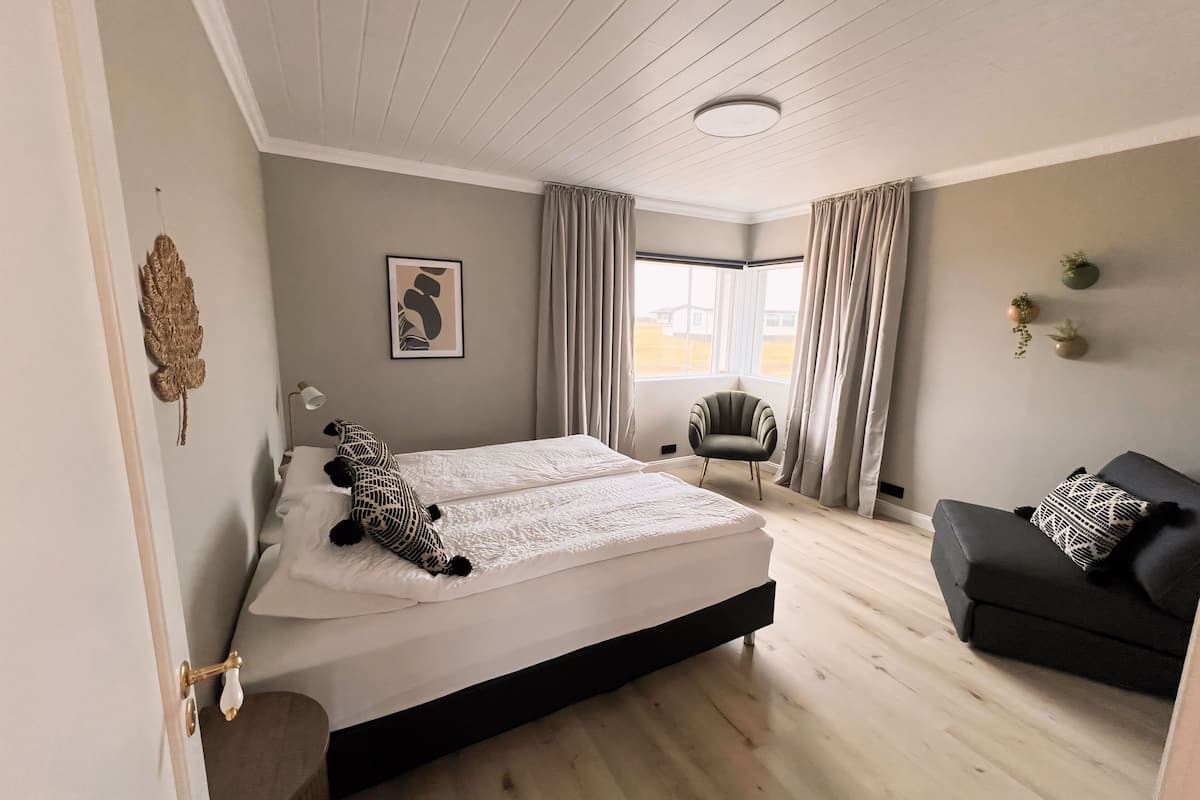 A bedroom with a bed, a chair, a sofa, a window, and a door.