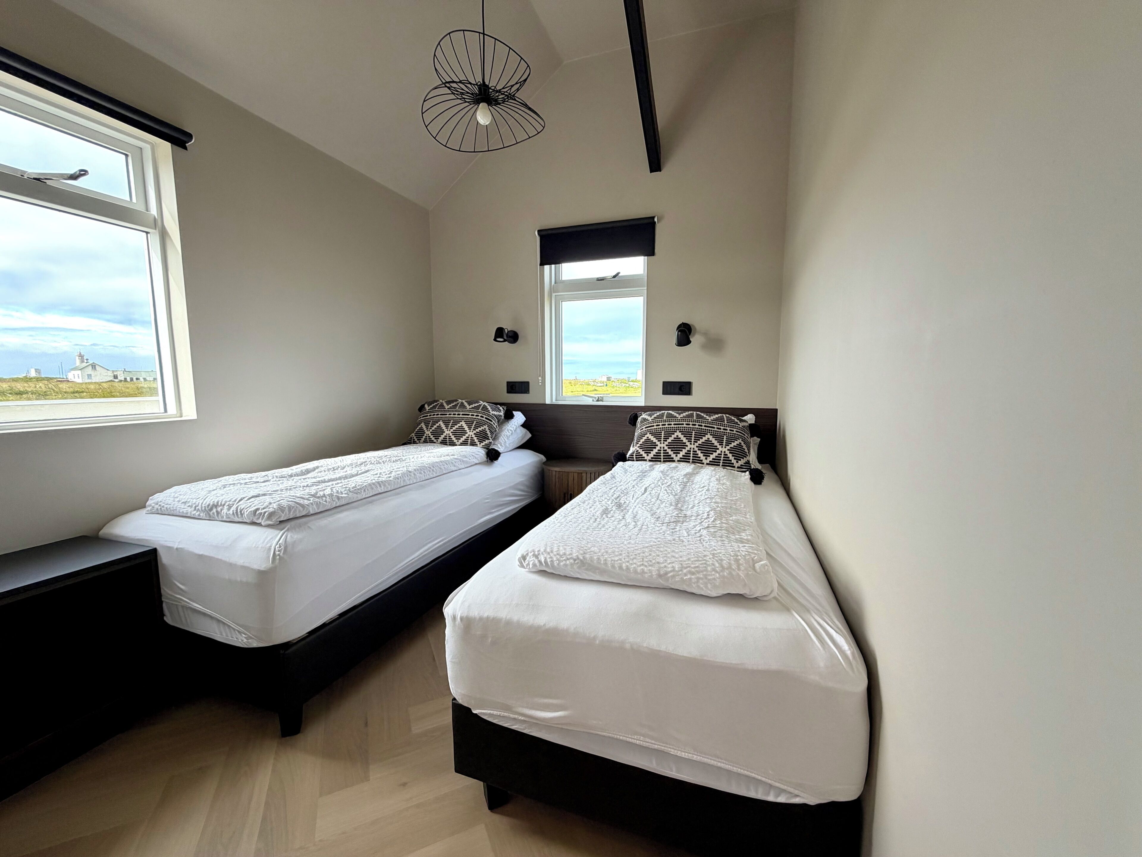 A bedroom with two beds, a window with a view, a pendant light, and a wall-mounted light fixture.