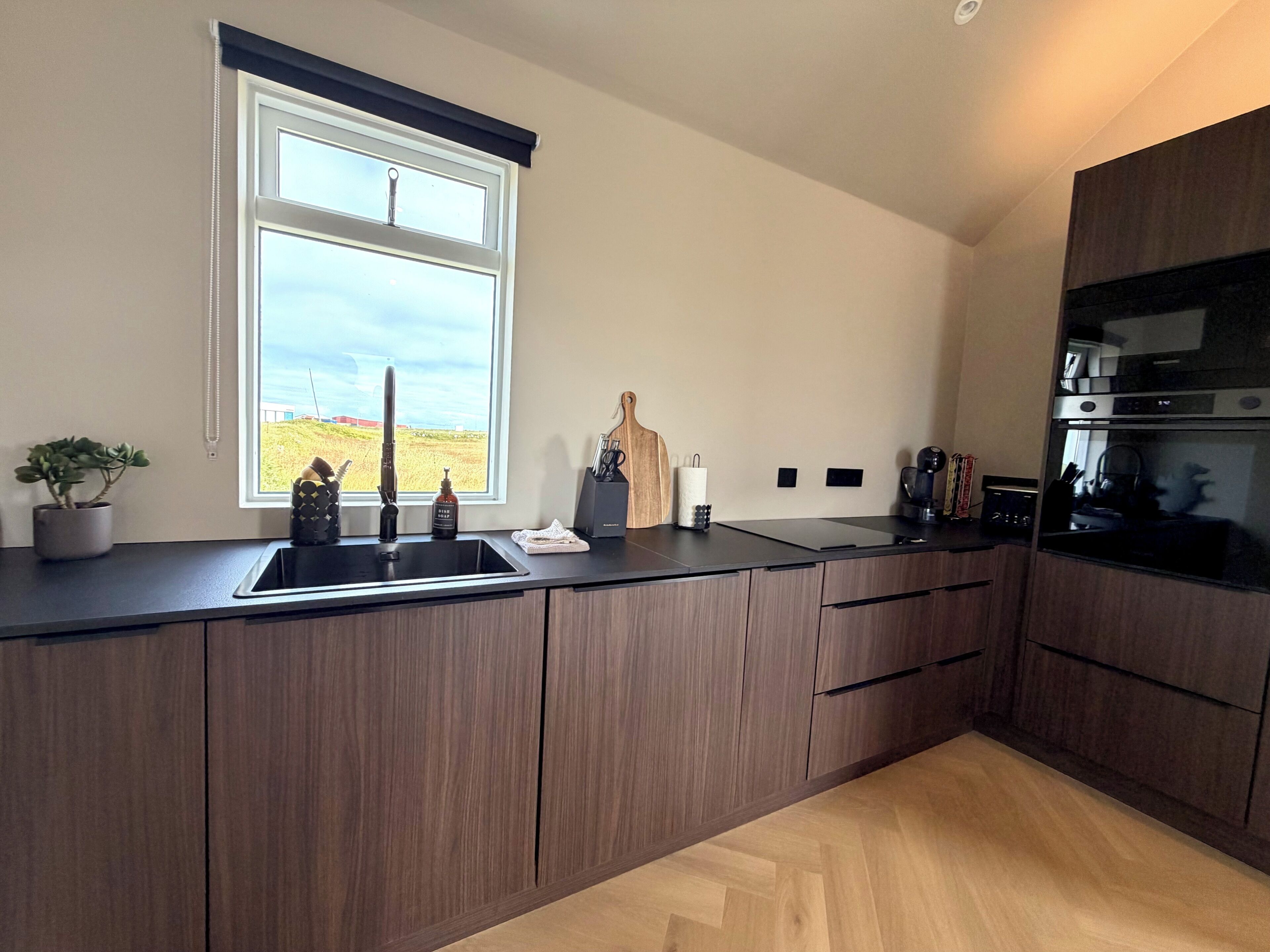 A modern kitchen with a large window, wooden cabinets, and a built-in oven.