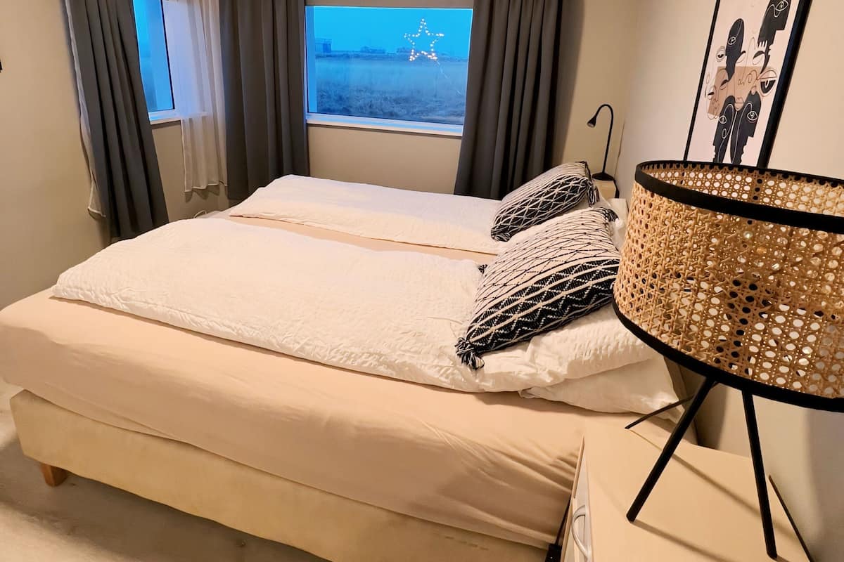 A bedroom with a large bed, two windows with curtains, a star decoration on the windowsill, and a framed picture on the wall.
