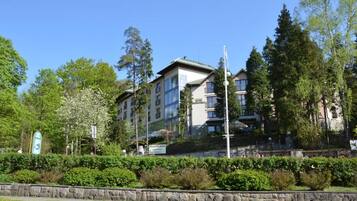 A multi-story residential building with balconies, surrounded by greenery and trees.