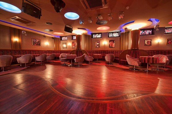 A spacious room with a curved wooden floor, multiple seating areas with cushioned chairs, and wall-mounted televisions.