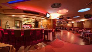 A bar area with a curved layout, bar stools, and a television screen. - Hotel Prezydent (Krynica-Zdroj)