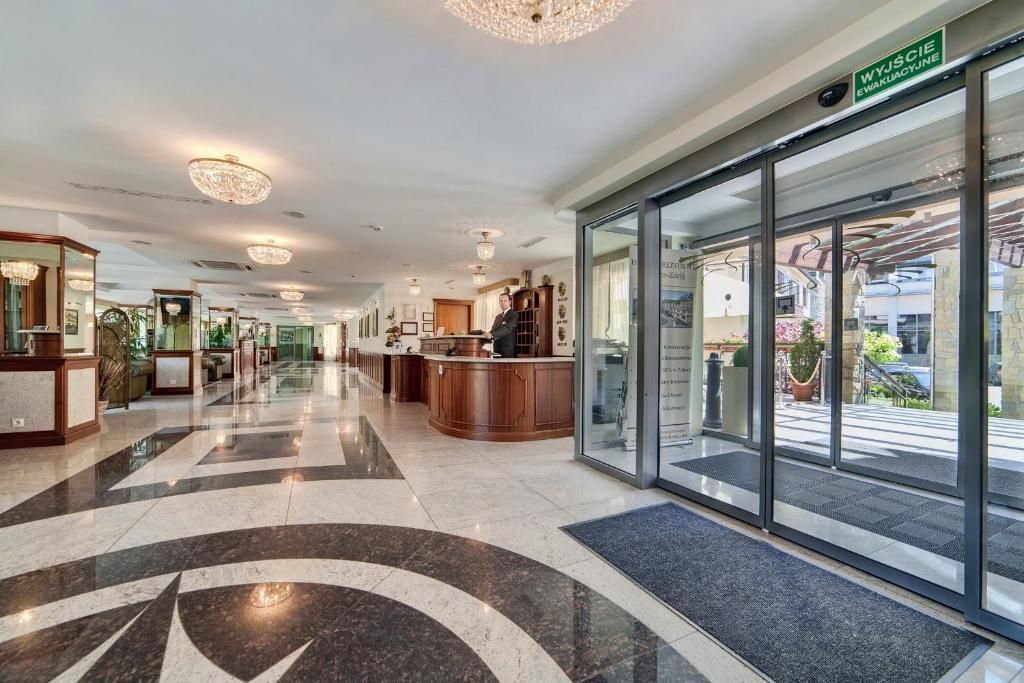 Un hall d’hôtel comprenant un comptoir d’accueil, une grande entrée vitrée et un lustre moderne.