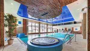 An indoor swimming pool with a hot tub, large windows, and a wooden ceiling. - Hotel Prezydent (Krynica-Zdroj)