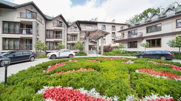 Un hotel con varios pisos, estacionamiento exterior y un jardín central con flores rojas y blancas.
