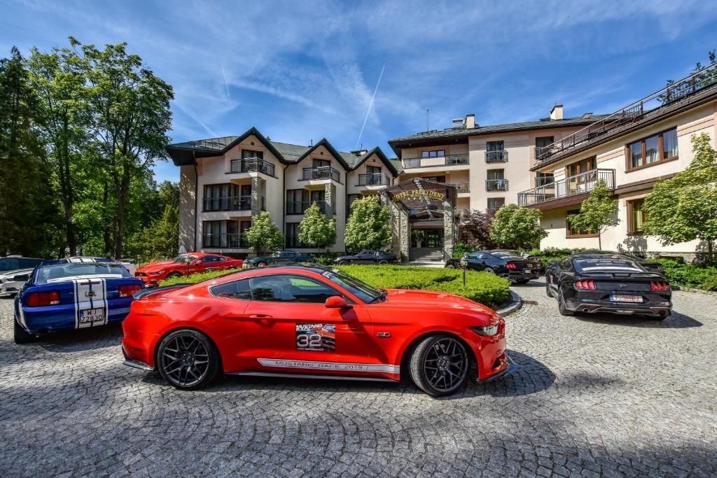 Un coche deportivo rojo estacionado frente a un edificio con varios balcones y cielo despejado.