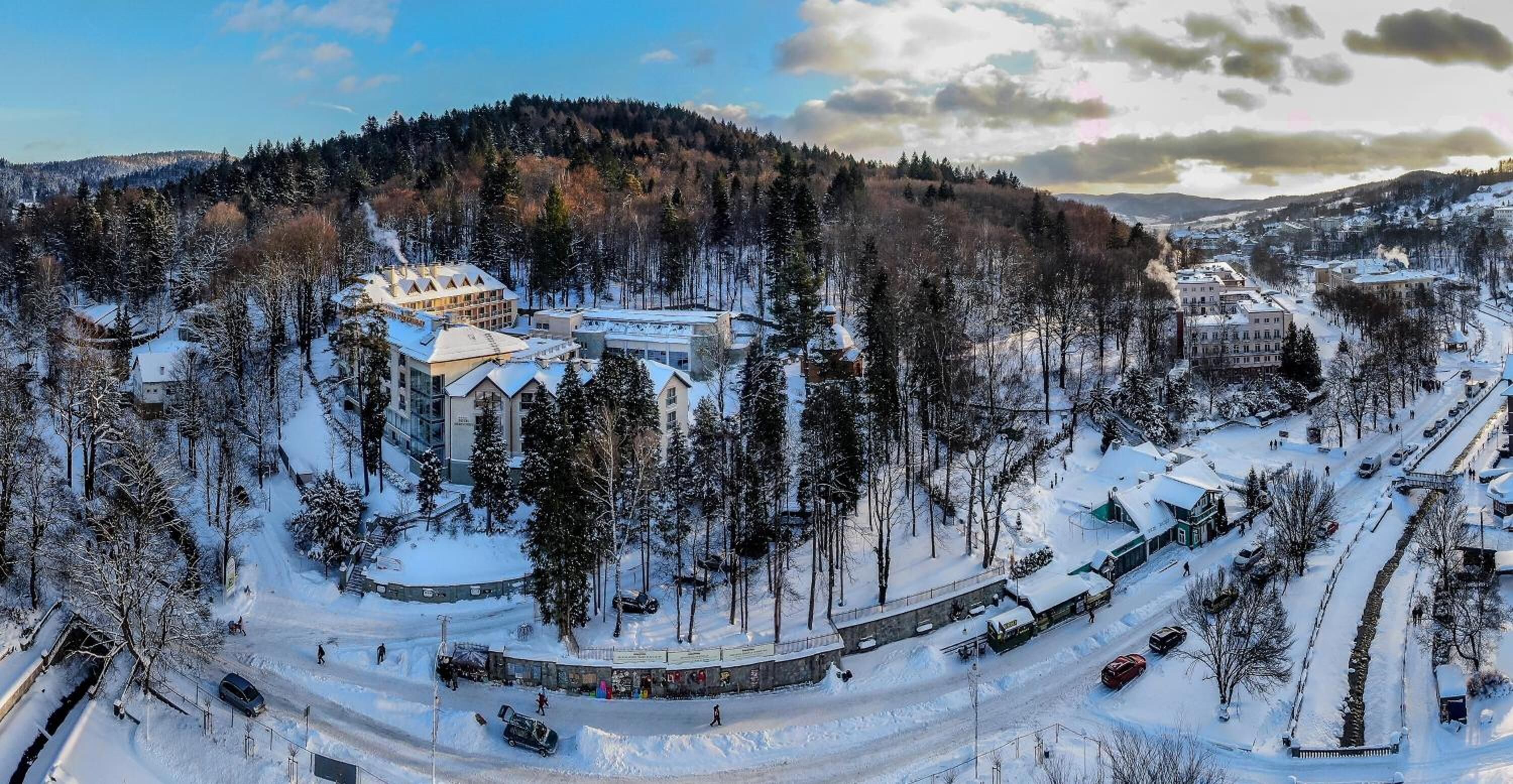Een besneeuwde plaats met een opvallend hotel in modern design, omringd door dichte bossen en een slingerende weg.
