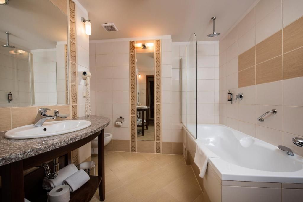 A modern bathroom with a sink, vanity, mirror, and bathtub.