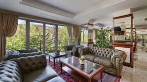 A spacious living room with leather sofas, a glass coffee table, and large windows offering a view of greenery outside. - Hotel Prezydent (Krynica-Zdroj)