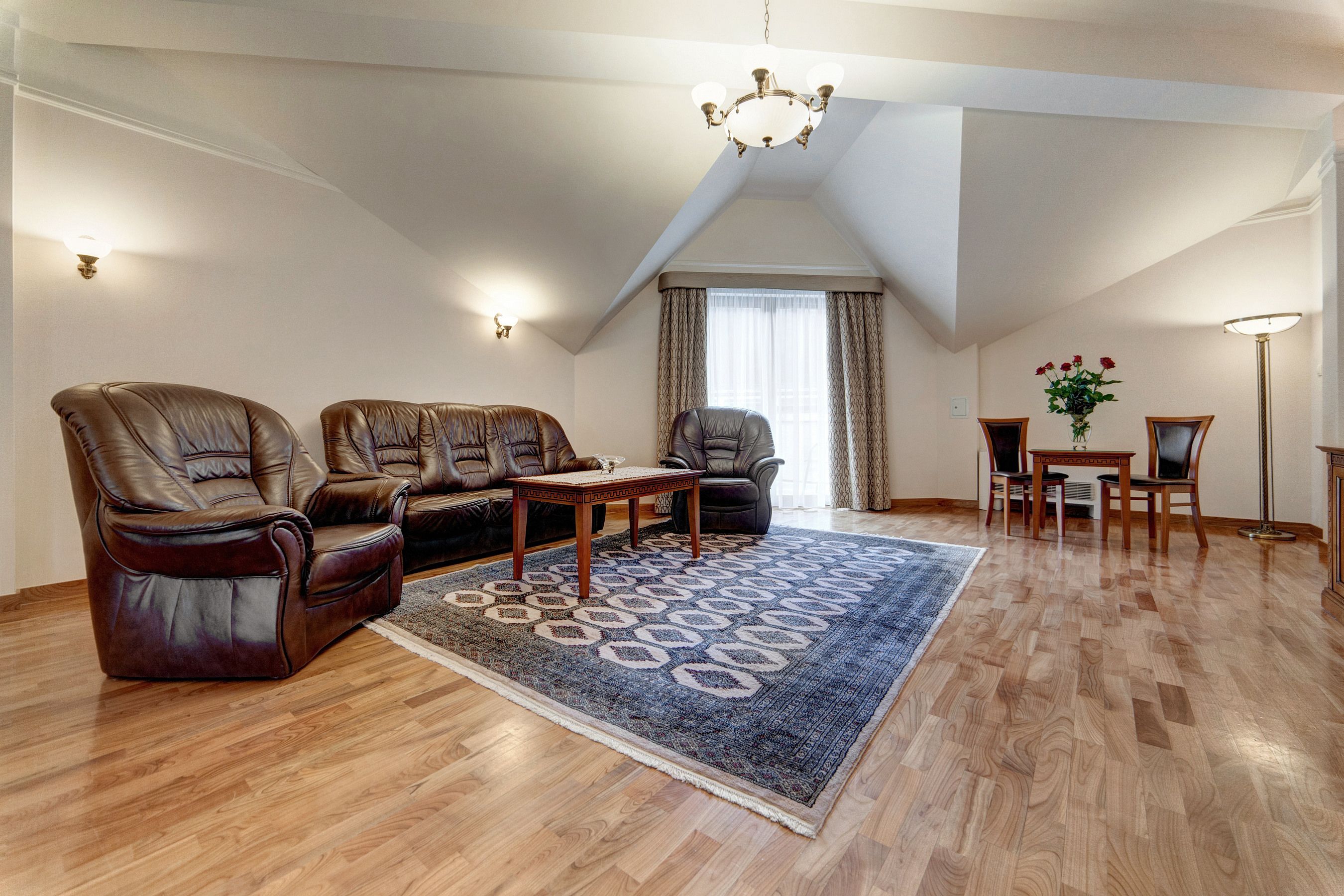 Ein geräumiges Wohnzimmer mit einer großen braunen Ledersofa, einem passenden Sessel und einem Couchtisch aus Holz. Ein gemustertes Teppich bedeckt den Holzboden.