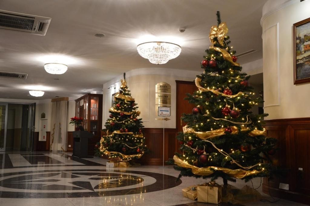 A lobby with two Christmas trees, a chandelier, and a reception desk.