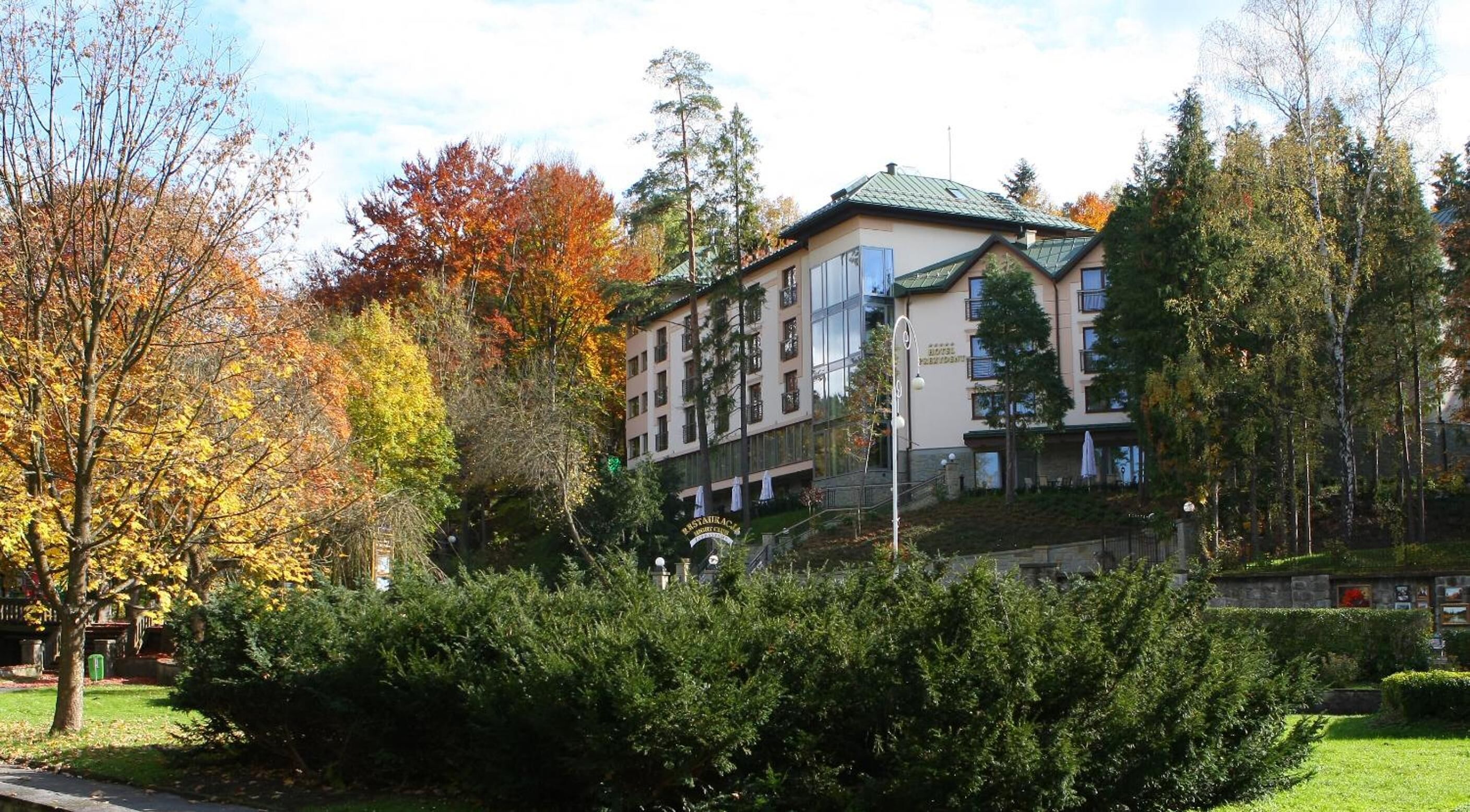 A multi-story hotel with a green roof, surrounded by trees with autumn foliage.