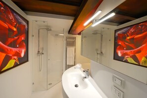 Un baño moderno con un lavabo blanco, cabina de ducha de vidrio y dos espejos grandes.