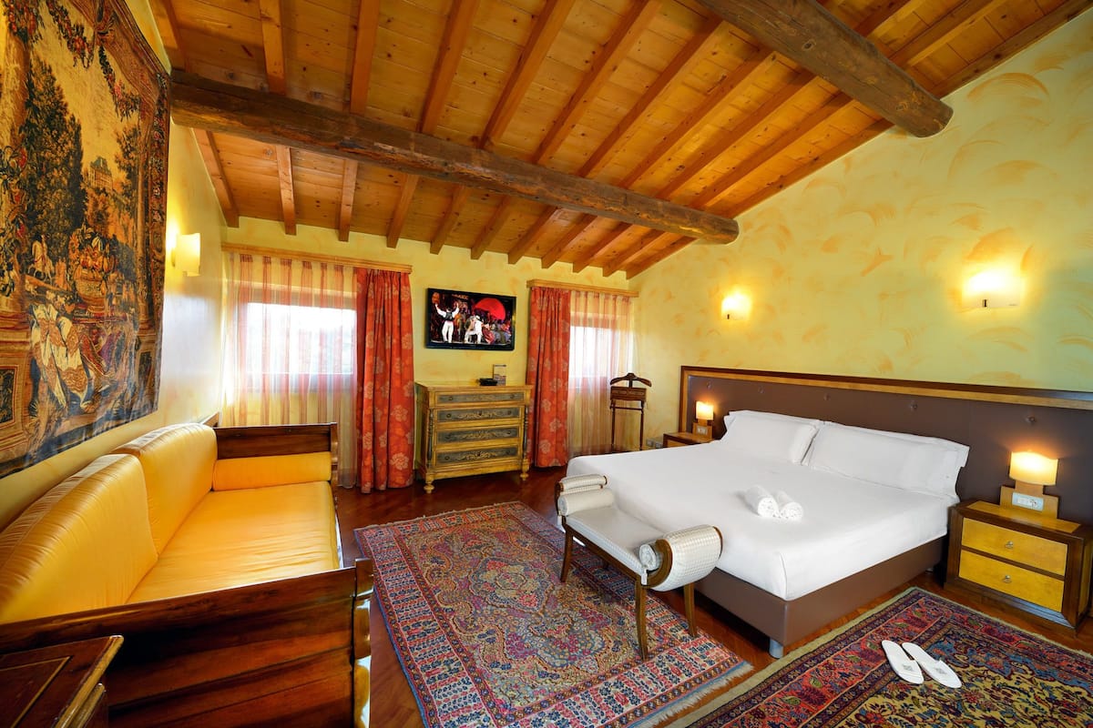 A traditional room with a wooden ceiling, a bed with white linens, a wooden dresser, a chair, a patterned rug, and a tapestry on the wall.