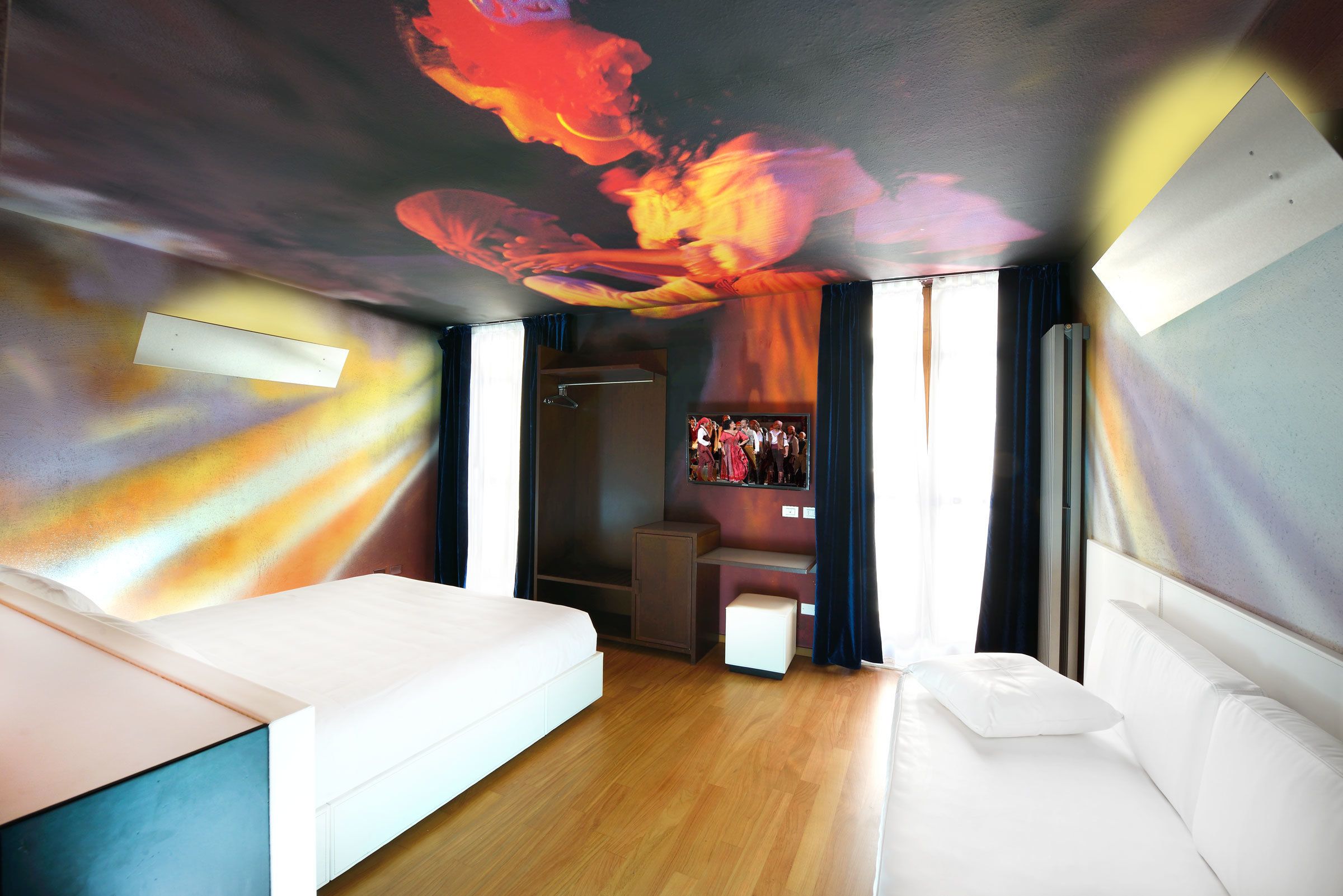 A modern hotel room with a large bed, a desk, and a wardrobe.