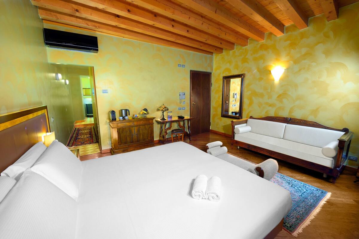 A hotel room with a large bed, a sofa, a wooden cabinet, and a mirror.