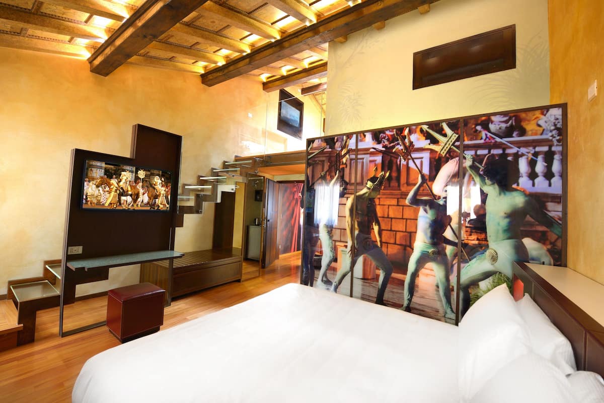 A hotel room with a large bed, a flat-screen TV, and a mural of dancers.