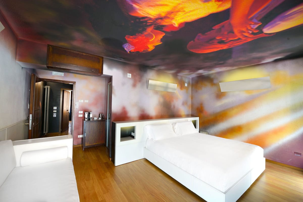 A modern hotel room with a large bed, a desk, and a ceiling mural.