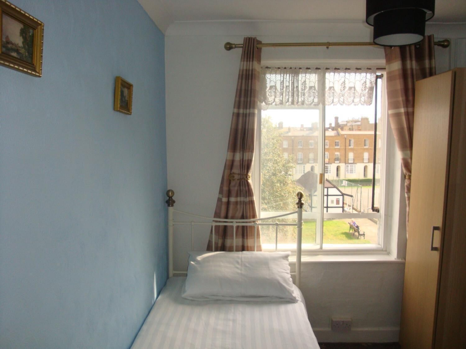 A bedroom with a single bed, a window with curtains, a view of the outside, and a door.
