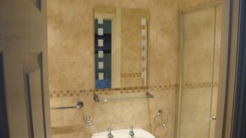 A bathroom with a white sink, a mirror, and a glass shelf above it.