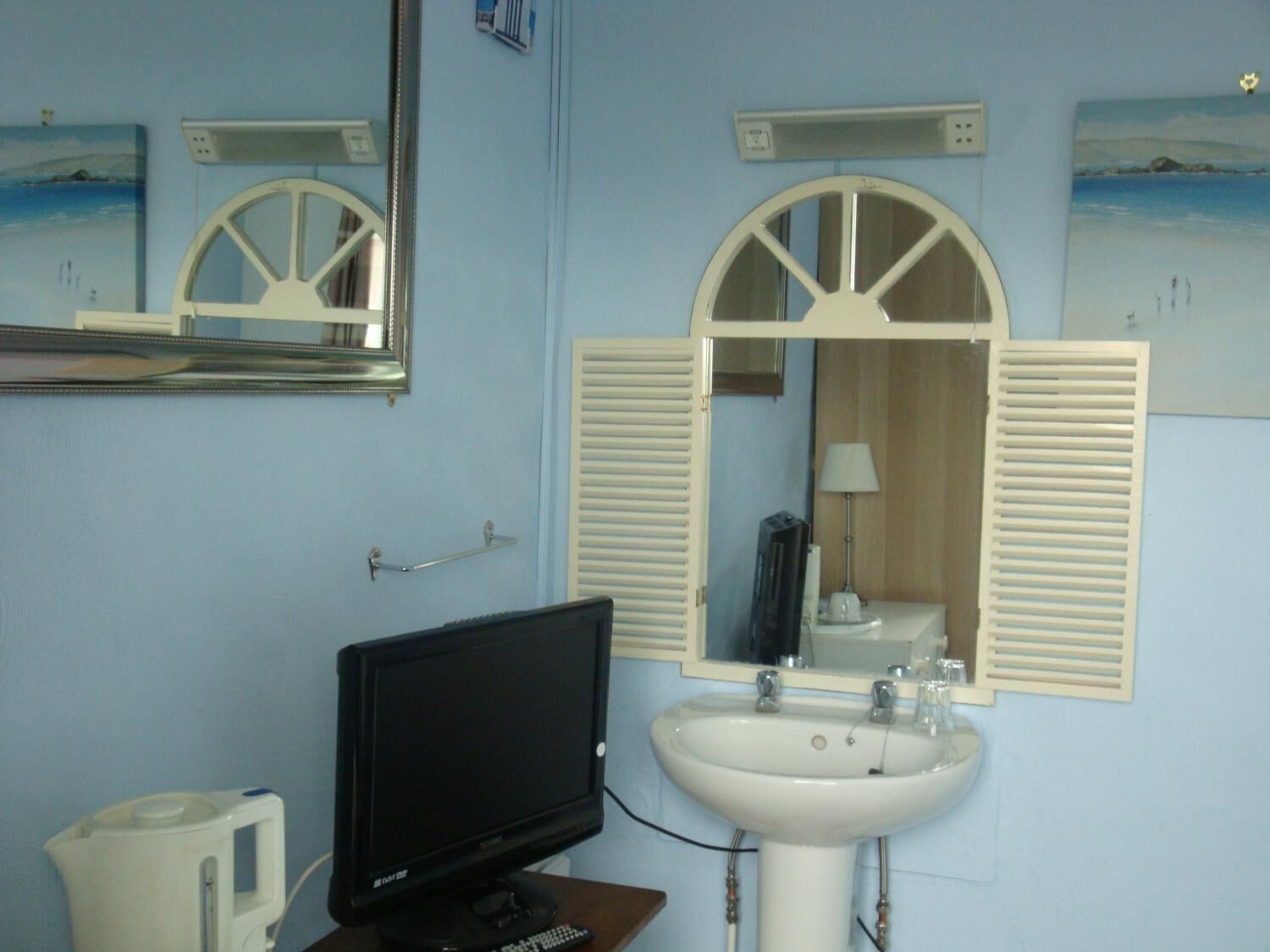 A bathroom with a sink, mirror, and a television on a stand.