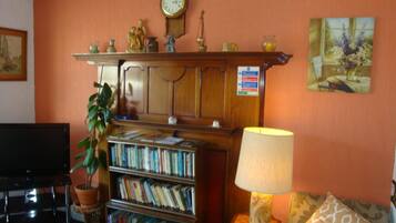 Un salon avec une bibliothèque, une horloge, une lampe et un tableau accroché au mur.