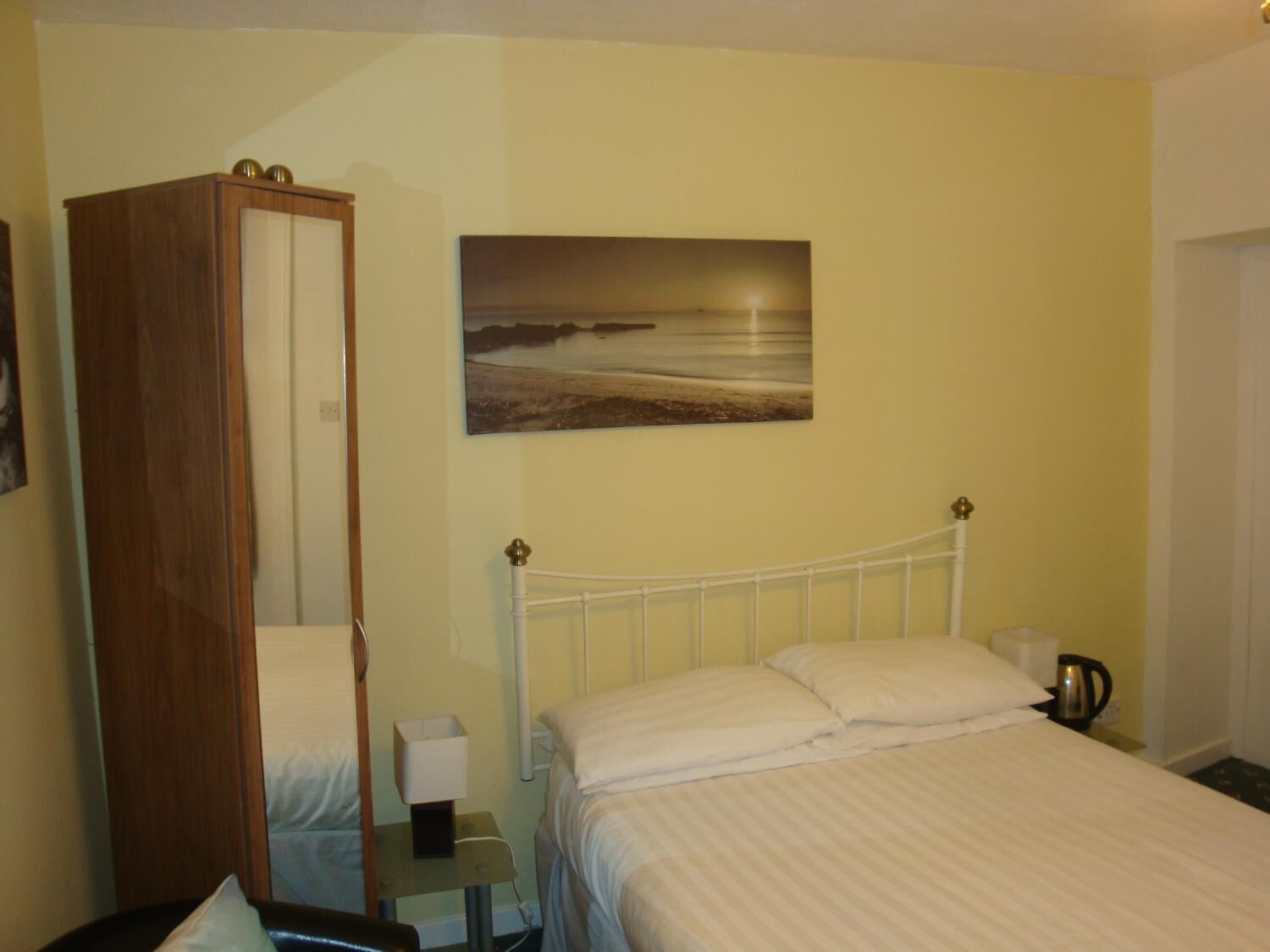 A bedroom with a bed, a nightstand, a bedside table, a wardrobe, and a painting of a beach scene.