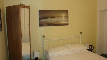 Une chambre à coucher comprenant un lit, une table de chevet, une commode, une armoire et un tableau représentant une scène de plage.