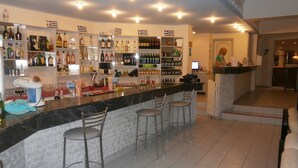 A bar area with a marble countertop, multiple shelves with bottles, and bar stools. - Aslanis Village Hotel (Kos)