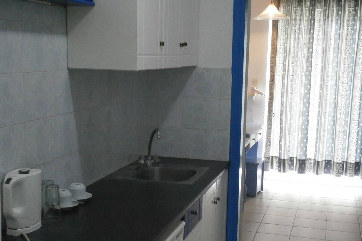 A small kitchen with a sink, a coffee maker, and a window with curtains.
