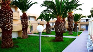 A courtyard with palm trees, a pathway, and a building with balconies. - Aslanis Village Hotel (Kos)