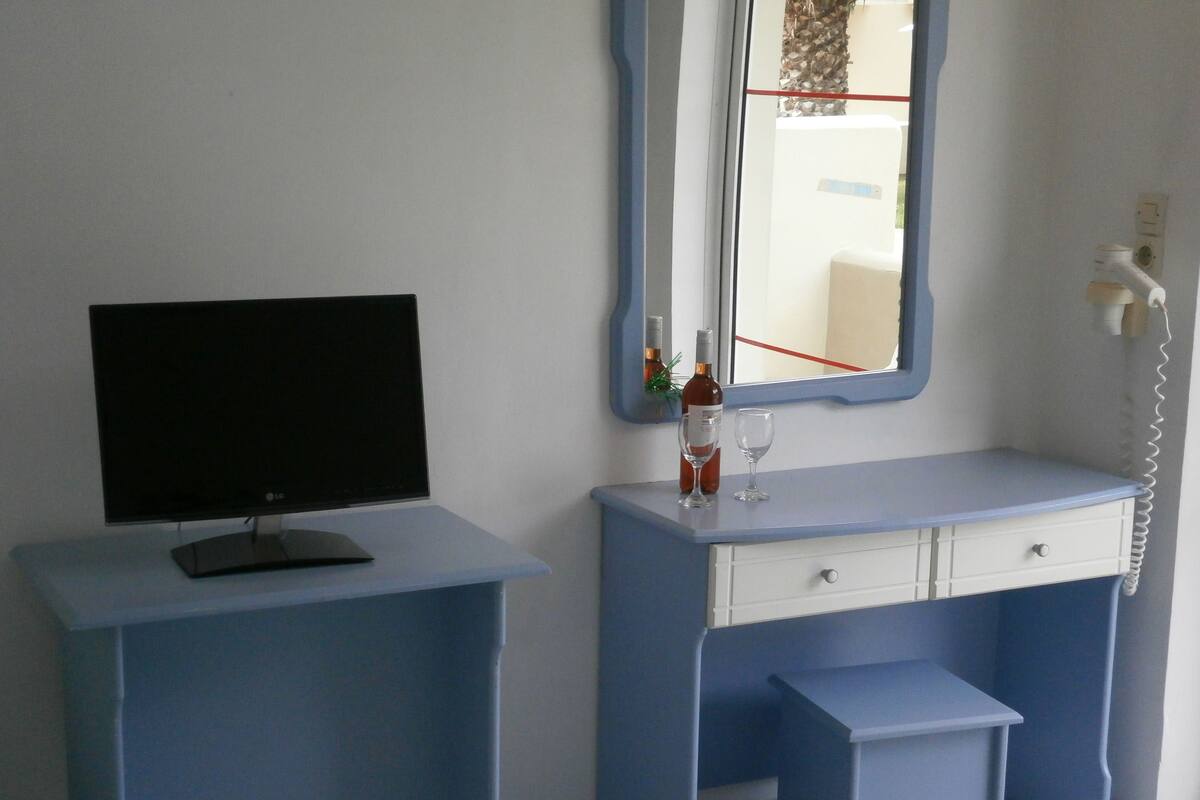A room with a TV on a stand, a mirror above a dresser, and a telephone on the wall.