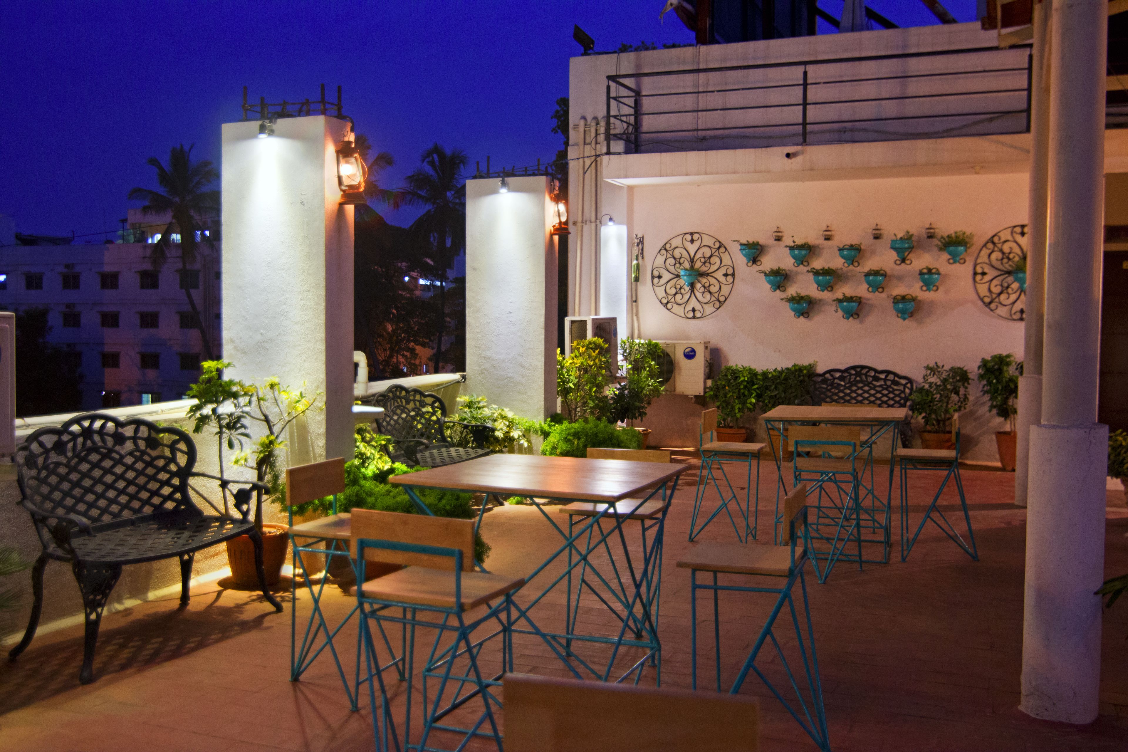 An outdoor patio area with tables and chairs, potted plants, and decorative wall art.