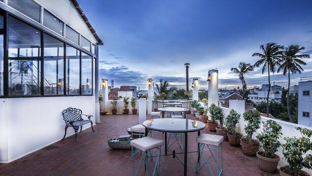 An outdoor terrace with a table and chairs, potted plants, and a bench. - Aishwarya Residency (Mysore)