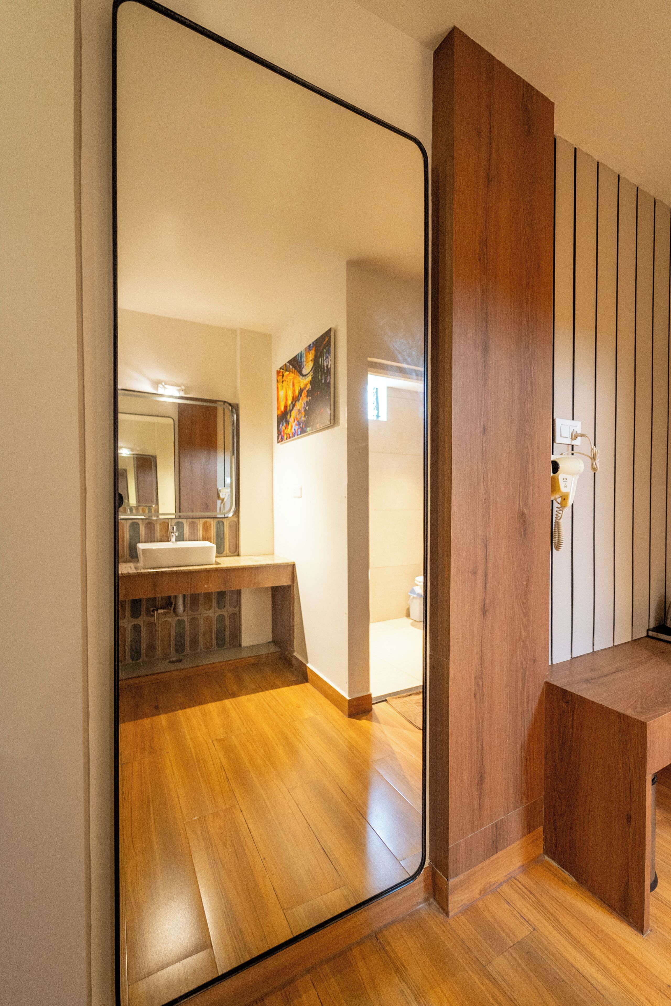 A modern bathroom with a wooden vanity, a large mirror, and a wooden floor.