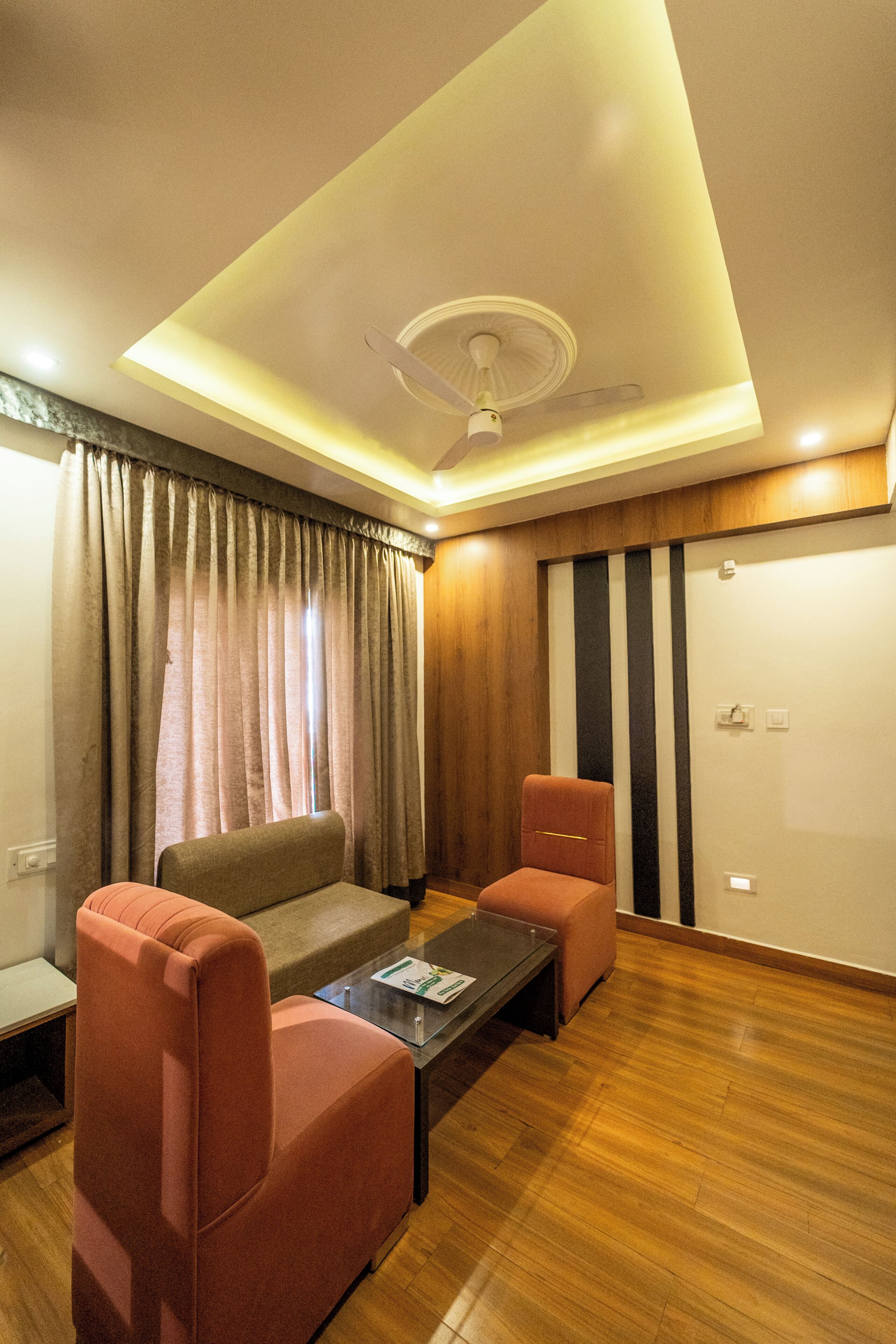 A room with a ceiling fan, a sofa, two armchairs, a coffee table, and a wooden floor.