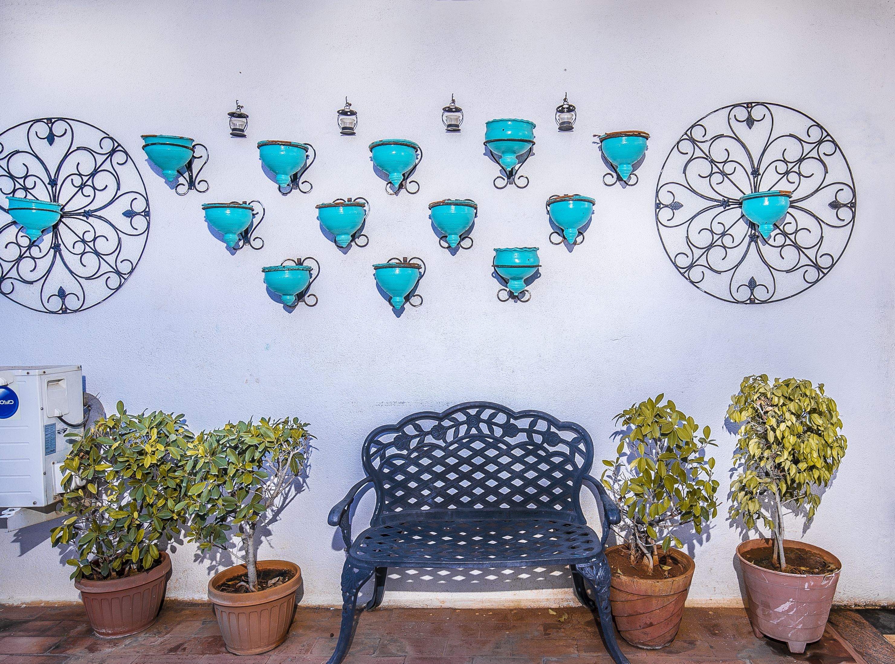 Un banco con plantas en macetas, una pared con apliques decorativos y un cuadro eléctrico.
