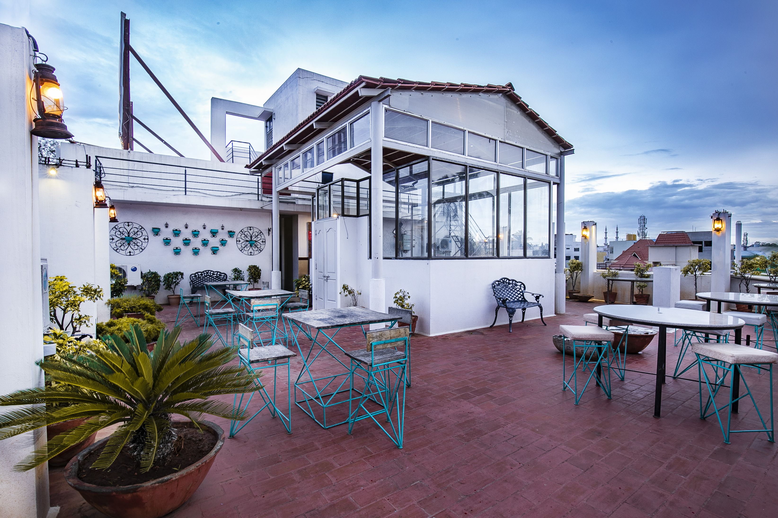 An outdoor patio with tables and chairs, potted plants, and a large glass enclosure.