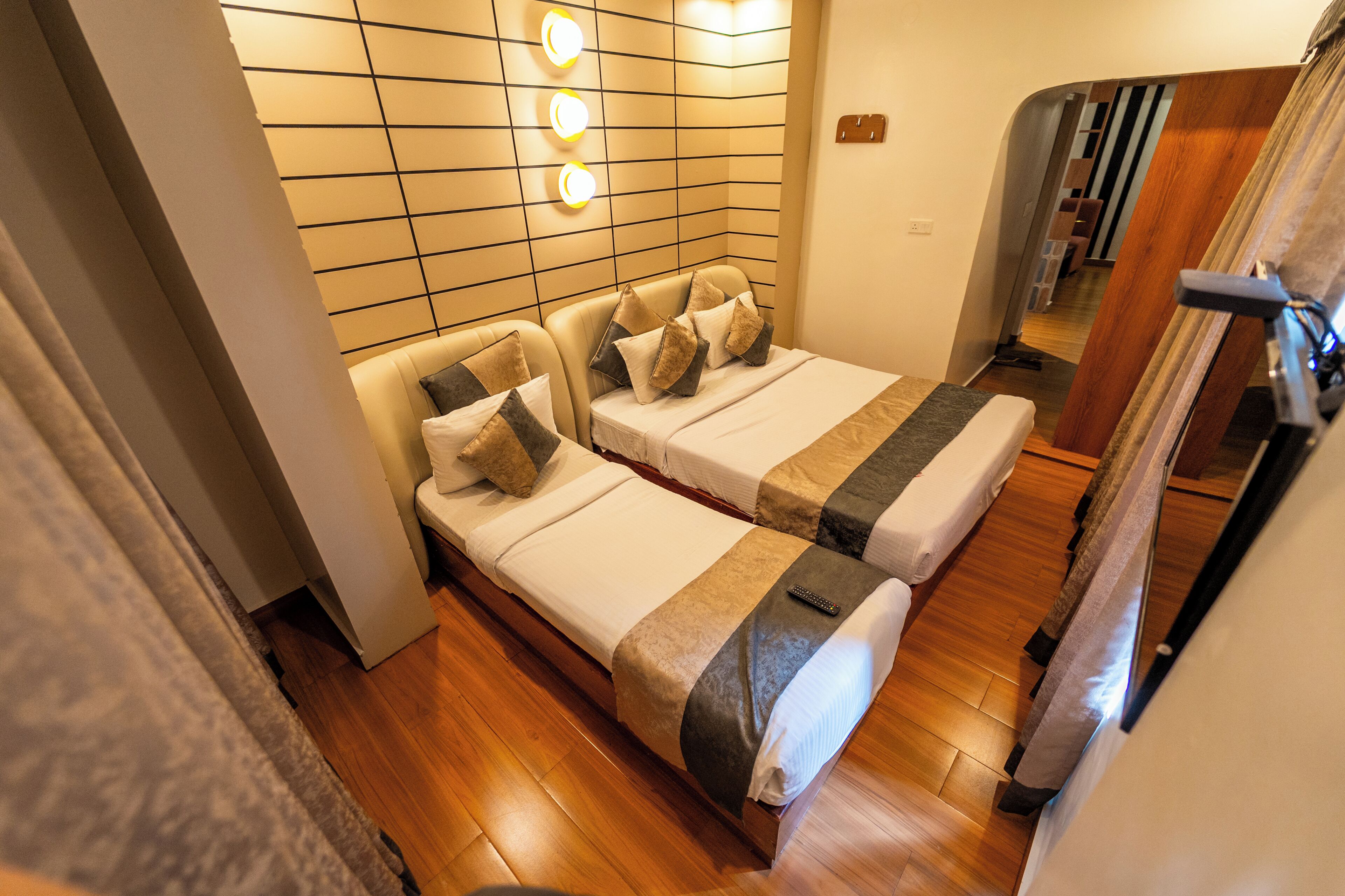 A hotel room with two beds, wooden flooring, a wall-mounted light fixture, and a mirror.