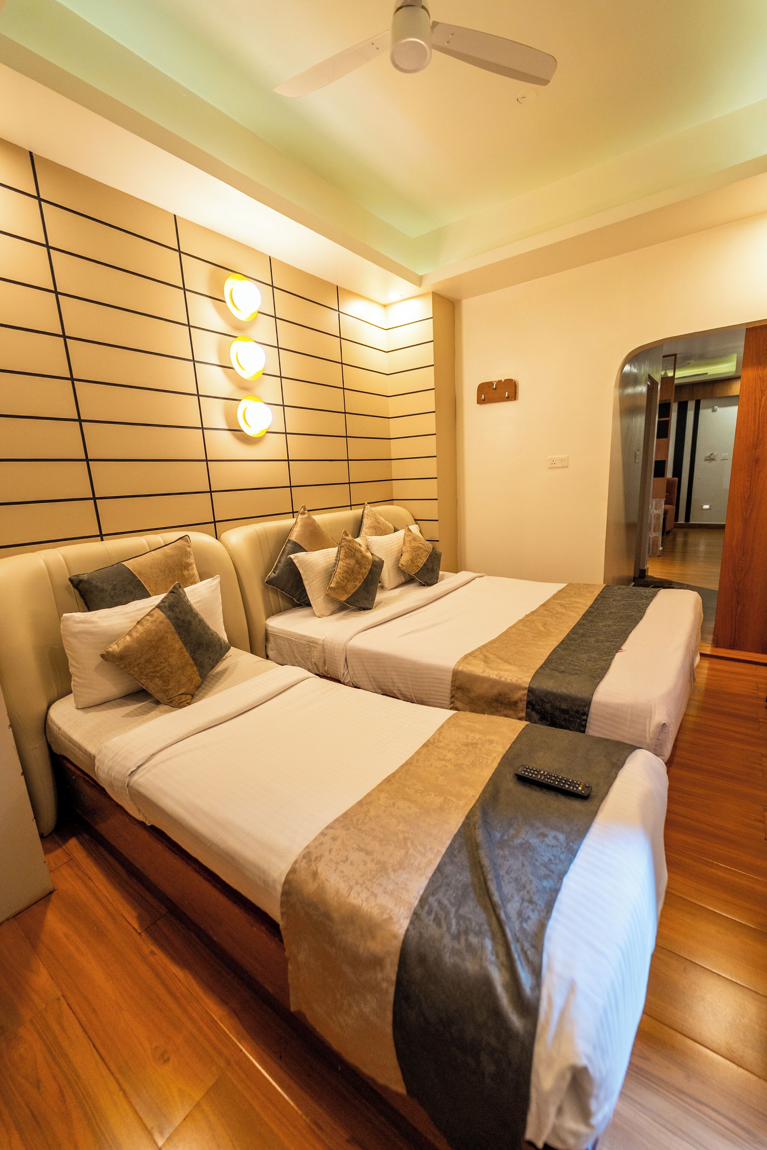Habitación de hotel con dos camas, un ventilador de techo y una lámpara fijada a la pared.