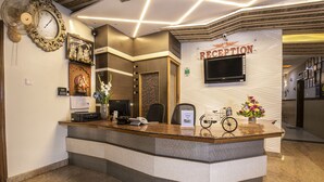 A reception desk with a clock, a TV, and a sign that reads "RECEPTION". - Aishwarya Residency (Mysore)