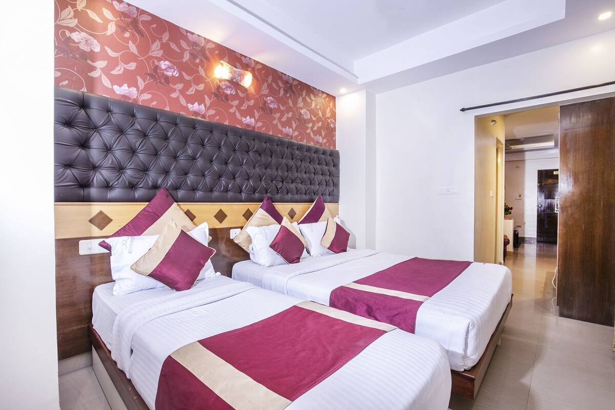 Habitación de hotel con dos camas, cabecera capitonada, papel tapiz floral y puerta de madera.