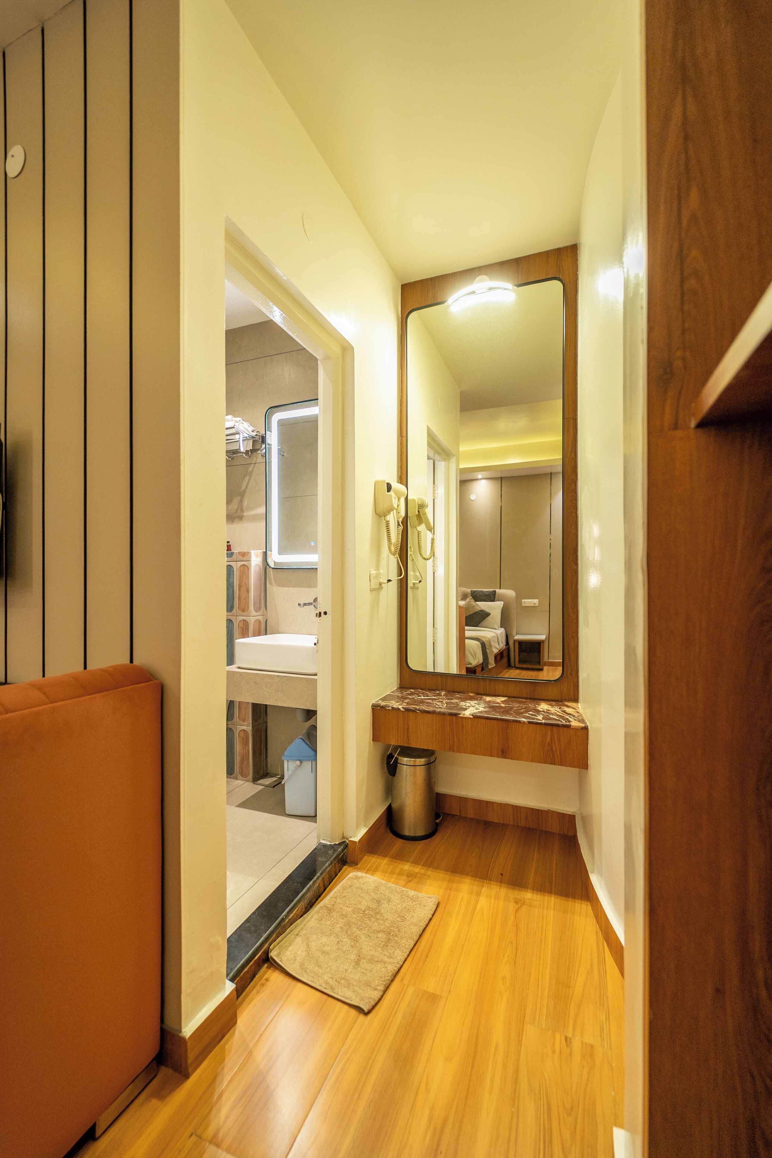 Un couloir avec un plancher en bois, un miroir, un lavabo et un petit tapis.
